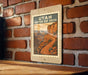 A framed poster of the scenic Utah Canyon Rim Drive, featuring a winding road and a mountainous landscape, is displayed on a brick wall.