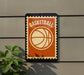 a basketball-themed sign with a stamp-like design, mounted on a wall next to a plant.