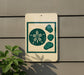 a sign with a beach-themed design, including a flower and four pebbles, mounted on a wall.