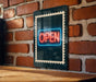 A neon sign that reads "OPEN" is displayed on a brick wall, mounted on a wooden surface.