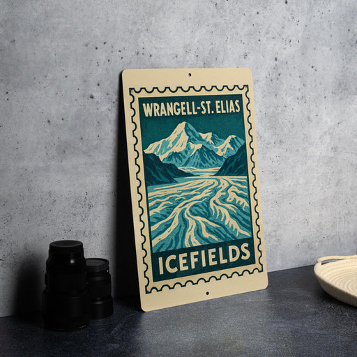 A metal sign with a mountain landscape and a river, featuring the text "WRANGEL-ST. ELIAS ICEFILES" on it, is displayed on a table next to some black camera lenses.