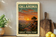 A framed poster of a sunset landscape with mountains and trees, titled "OKLAHOMA" and "SUNSET Vista Point", is displayed on a shelf next to a wooden cutting board and a potted plant.