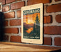 A vintage-style sign for the Sunset Vista Point in Colorado, featuring a scenic landscape with pine trees and a sunset over a mountain range.