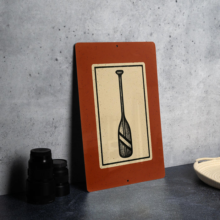 a red sign with a black and white illustration of a paddle, placed on a gray countertop next to a stack of black camera lenses.