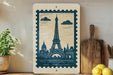 a framed print of the Eiffel Tower on a shelf, surrounded by various kitchen utensils and a potted plant.