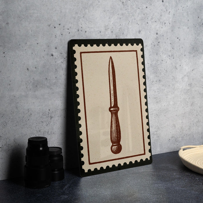 a framed picture of a knife with a brown border, placed on a countertop next to some black camera lenses.