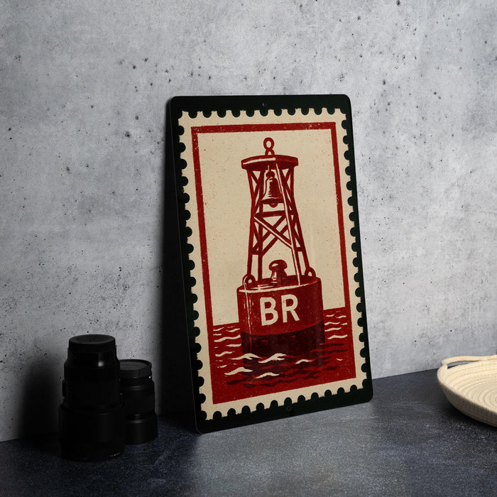 A framed image of a red and white lighthouse with the letters "BR" on it, placed on a gray countertop next to some black camera lenses.