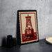 A framed image of a red and white lighthouse with the letters "BR" on it, placed on a gray countertop next to some black camera lenses.