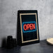a black frame with a neon sign that says "OPEN" in red and blue colors, placed on a table next to some black camera lenses.