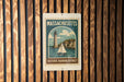 A metal sign with a vintage-style illustration of a lighthouse and a small sailboat, mounted on a wooden wall.