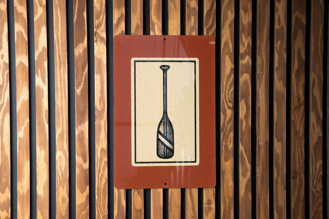 a sign with a paddle on it, mounted on a wooden wall.