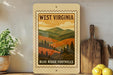 A framed vintage-style poster of West Virginia, featuring a mountain landscape with pine trees, is displayed on a shelf next to a wooden cutting board and a potted plant.