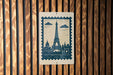 A blue postage stamp featuring the Eiffel Tower is displayed on a wooden wall.