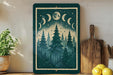 a framed illustration of a forest scene with pine trees and a crescent moon, displayed on a shelf next to a wooden cutting board and a potted plant.