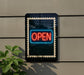 A neon "OPEN" sign is displayed on a wall, with a plant visible to the left side of the frame.
