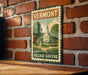 A vintage-style metal sign with the text "Vermont Village Greens" displayed on a brick wall.