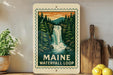 A framed illustration of a waterfall surrounded by pine trees, with the text "MAINE WATERFALL LOOP" below the image.