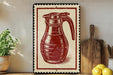 a red and white framed illustration of a coffee pot on a wooden shelf, with a potted plant and a wooden cutting board nearby.