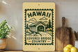 A wooden sign with a graphic of a covered bridge and the text "Hawaii Covered Bridge Country" is displayed on a shelf next to a potted plant and a cutting board.