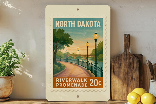 A framed poster of a scenic riverwalk promenade in North Dakota, featuring a path lined with trees and lampposts, with a sunset in the background.