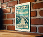 A metal sign with a graphic of a wooden walkway and the text "BARRIER ISLAND PATHWAYS" is mounted on a brick wall.
