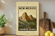 a framed poster of the Granite Peaks in New Mexico, with a wooden cutting board and a potted plant to the left.