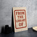 a sign that reads "FROM THE LIBRARY OF" in bold red letters, placed on a gray countertop next to a stack of black camera lenses.