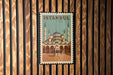 A framed poster of the Blue Mosque, a famous landmark in Istanbul, Turkey, is displayed on a wooden wall.
