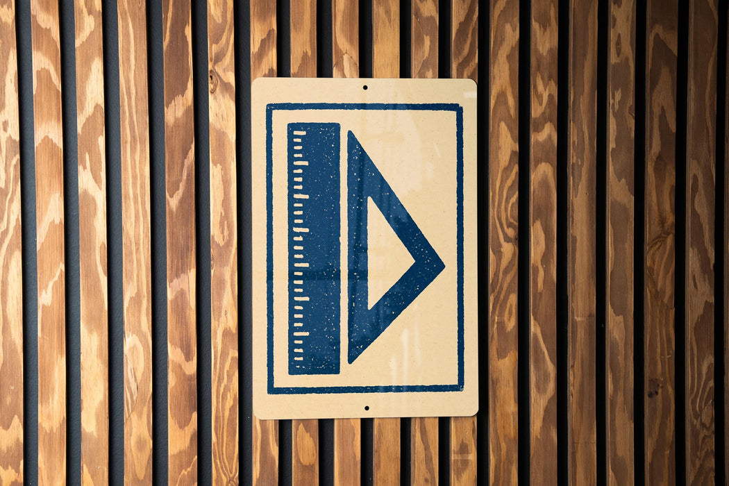 a sign with a blue triangle and a ruler on it, mounted on a wooden wall.
