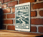 A sign for Barrier Island Pathways in Alaska is displayed on a brick wall.