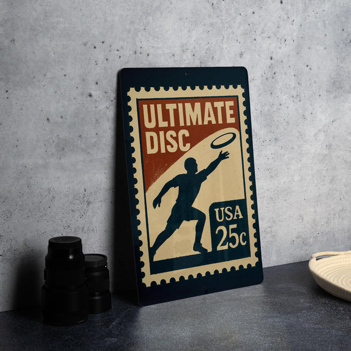 A vintage-style metal sign with a silhouette of a person playing frisbee, along with text indicating it is a "Ultimate Disc" and is a "USA 25c".