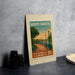 A framed poster of a riverwalk promenade in North Dakota, featuring a scenic image of a path lined with lampposts and trees.
