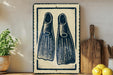 a framed artwork of two blue and white fins, placed on a shelf next to a wooden cutting board and a potted plant.