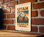 A metal sign with the text "UTAH GRAINITE PEAKS" is displayed on a brick wall.