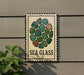 a sign with a sea glass design, mounted on a wall next to a plant.