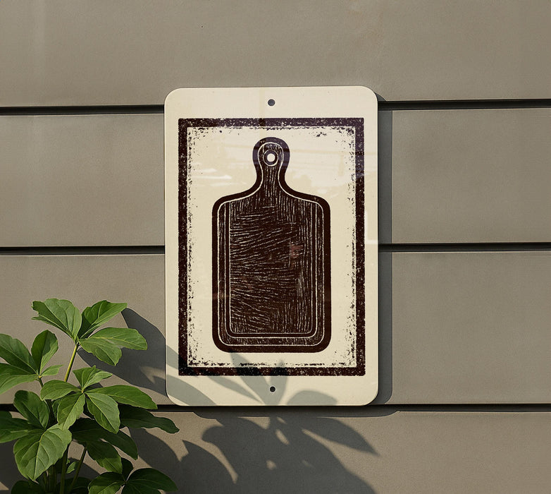 a white sign with a black silhouette of a cutting board, mounted on a wall next to a plant.