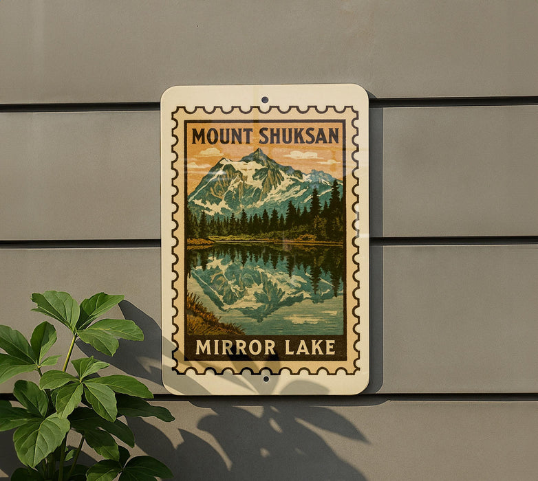 A vintage-style metal sign with a mountain landscape and a lake, mounted on a gray wall.