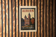 A vintage-style postage stamp from Alabama featuring a building with a clock tower, mounted on a wooden wall.