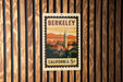 A vintage postage stamp from California, featuring a cityscape and a tower, is displayed on a wooden wall.