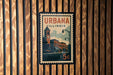A vintage postage stamp from Illinois, featuring a building and a clock, is displayed on a wooden wall.
