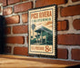 A vintage-style postage stamp from Pico Rivera, California, featuring a building and palm trees, is displayed on a brick wall.