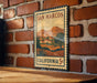 A vintage-style metal sign with a landscape illustration and text, mounted on a brick wall.