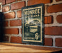 A vintage-style postage stamp from Louisiana, featuring a bridge and water, is displayed on a brick wall.