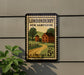 A vintage postage stamp from the United States, featuring a rural scene with a house, road, and trees, mounted on a wall.