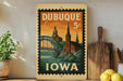 A vintage postage stamp from Dubuque, Iowa, featuring a bridge and a church, is displayed on a shelf next to a wooden cutting board and some lemons.