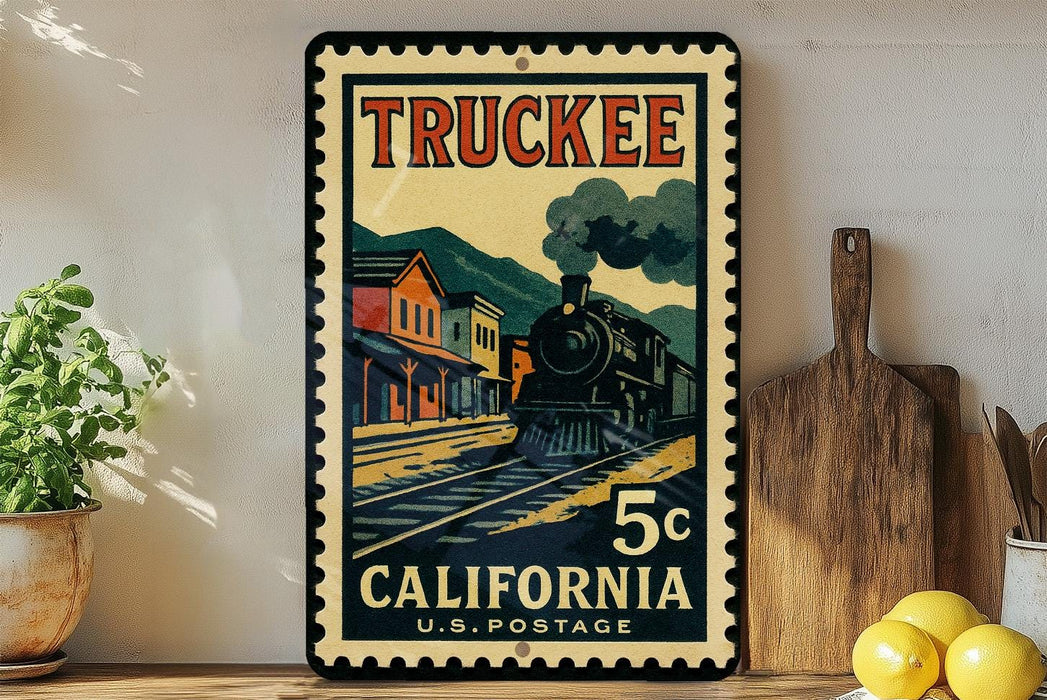A vintage-style postage stamp featuring a train on a track, with the text "TRUCKEE" and "5¢ CALIFORNIA U.S. POSTAGE" printed on it. The stamp is displayed on a wall, with a wooden cutting board and a potted plant visible in the foreground.