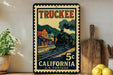 A vintage-style postage stamp featuring a train on a track, with the text "TRUCKEE" and "5¢ CALIFORNIA U.S. POSTAGE" printed on it. The stamp is displayed on a wall, with a wooden cutting board and a potted plant visible in the foreground.