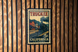 A vintage postage stamp from California, featuring a steam locomotive on the tracks, mounted on a wooden wall.