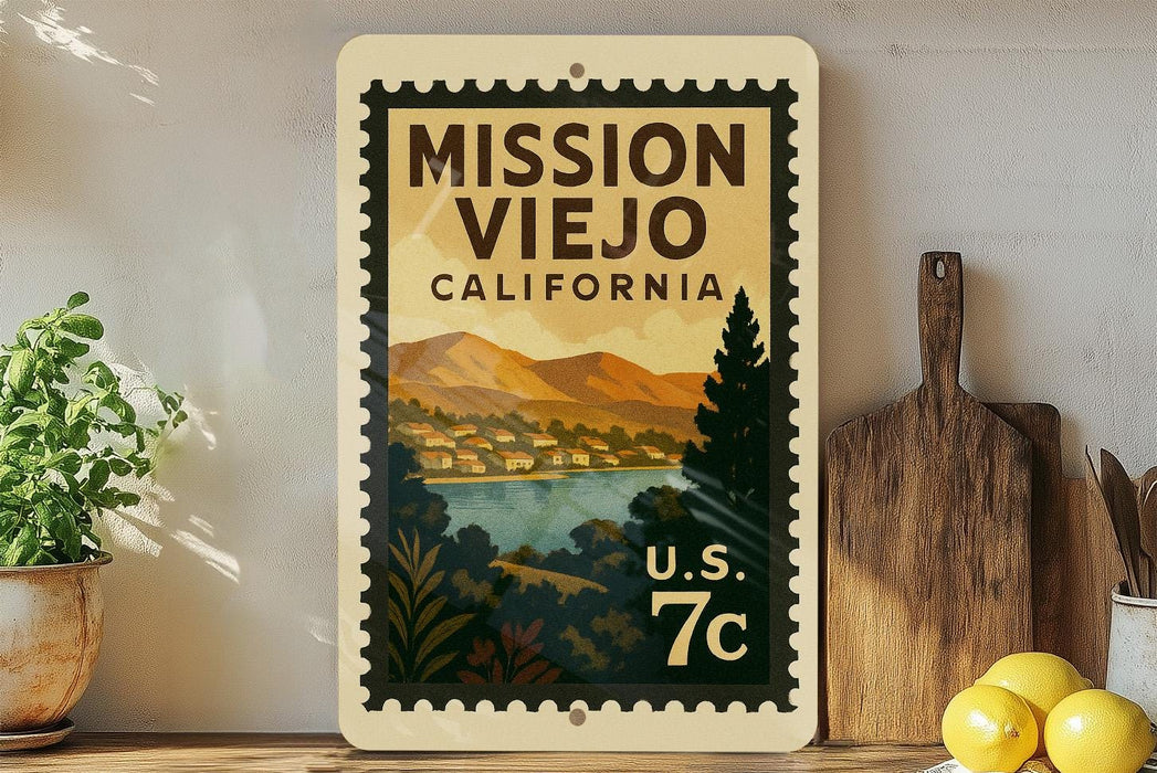 A vintage-style metal sign with a postage stamp design, featuring a scenic landscape of mountains, a river, and a town, mounted on a wall next to a wooden cutting board and some potted plants.