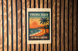 A vintage-style poster of Virginia Beach, featuring a palm tree, sunset, and ocean waves, is displayed on a wooden wall.